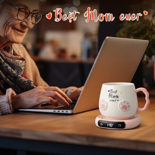 Elderly woman using laptop with 'Best Mom Ever' mug on warmer