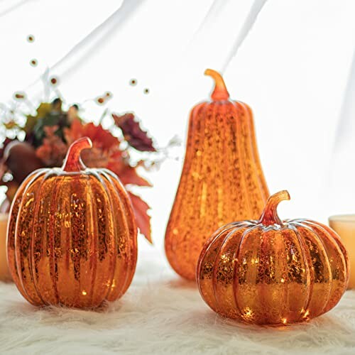 Glittering orange pumpkins and gourd on a white surface with autumn leaves.