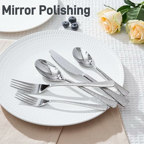 Mirror polished cutlery set on a white plate with roses and blueberries.