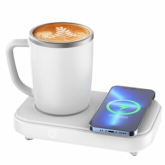 White mug with latte on a wireless charger next to a smartphone.