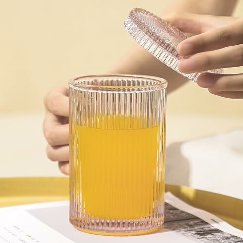 Hand holding lid of ribbed glass jar with orange juice