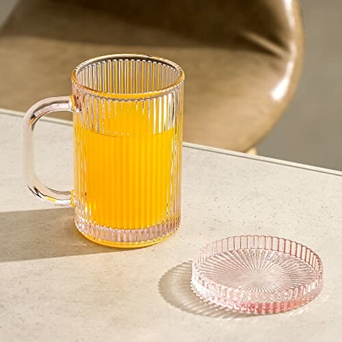 Ribbed glass mug with orange juice and a lid on a table.